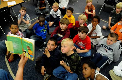 image of boys sitting on floor watching teacher who holds a book