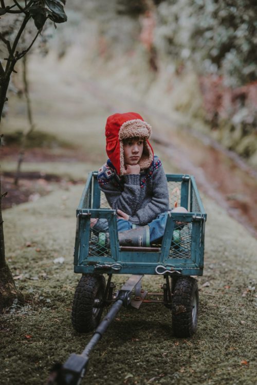 image of child wearing red ear-flap hat sitting in blue wagon
