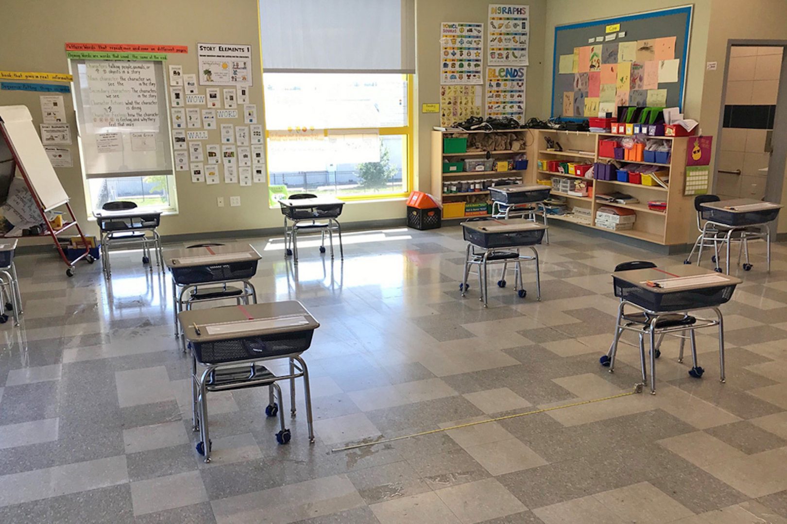 photograph of classroom with desks separated by six feet, whiteboards with material on two walls, window in the background